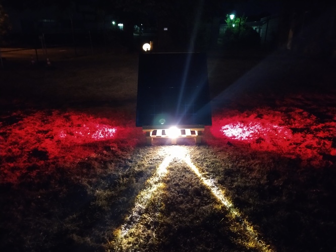 red and white lights coming out of an art installation with two solar modules in the night.
