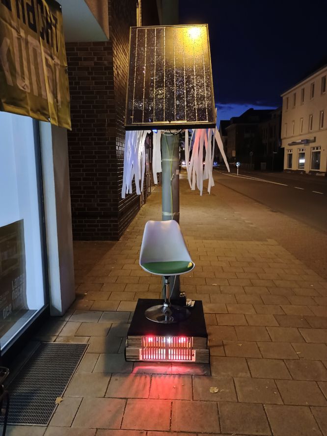 full image of outdoor solar installation in front of gallery. A chair and a solar panel.